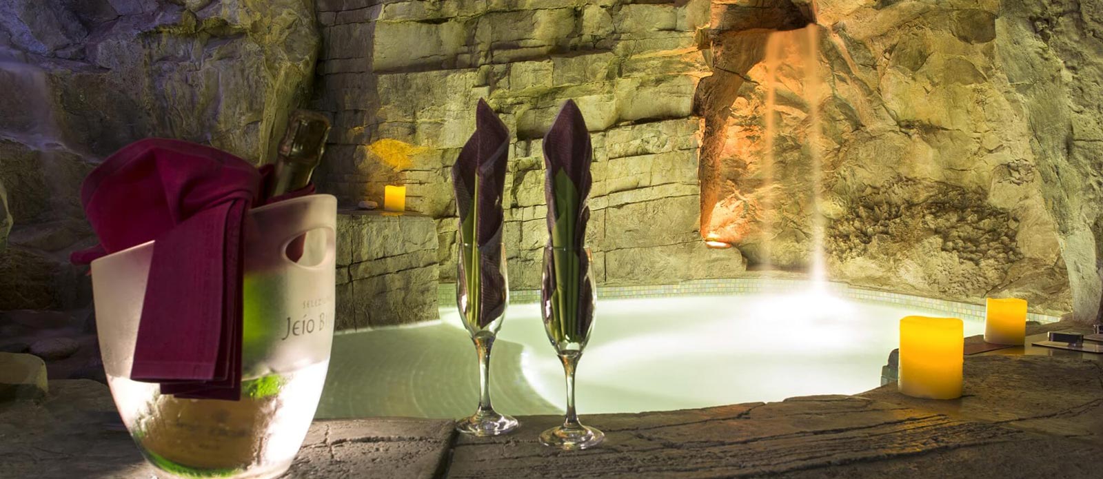 Motel K Wellness Suite Grotta Verde vista sulla mini piscina con idromassaggio e cascata, cromoterapia, bottiglia di champagne in secchiello del ghiaccio appoggiata a bordo piscina con 2 biccheri, servizio candele in suite camera a tema grotta verde di marina di andrano